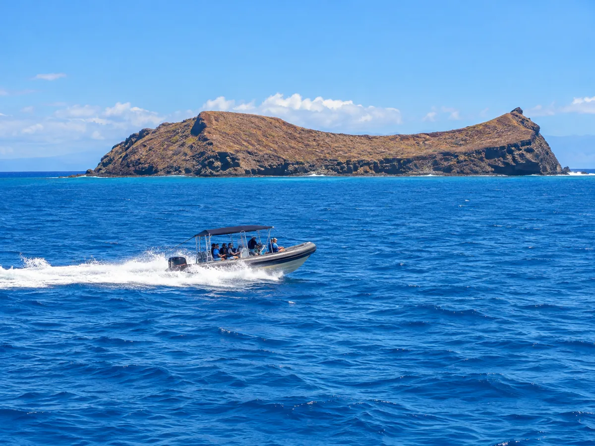 A small snorkel raft speeding across blue water toward the crescent of Molokini